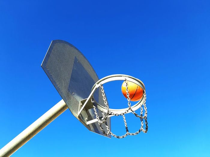 Low angle view of basketball hoop and ball against blue sky