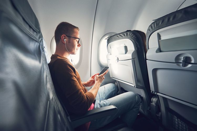 Man listening music while using mobile phone in airplane