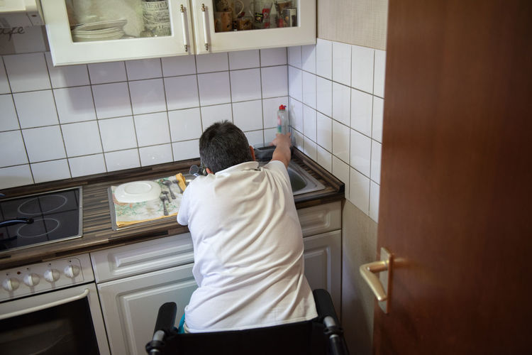 A disabled woman in a wheelchair washes dirty dishes