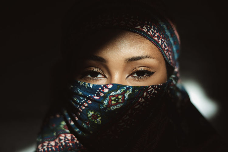 Close-up portrait of woman covering face against black background
