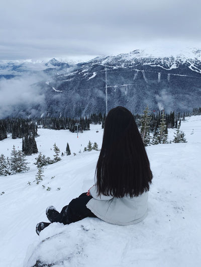 Rear view of woman sitting on snow covered land against mountain