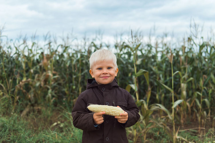 Cute happy child in corn field holding corncob