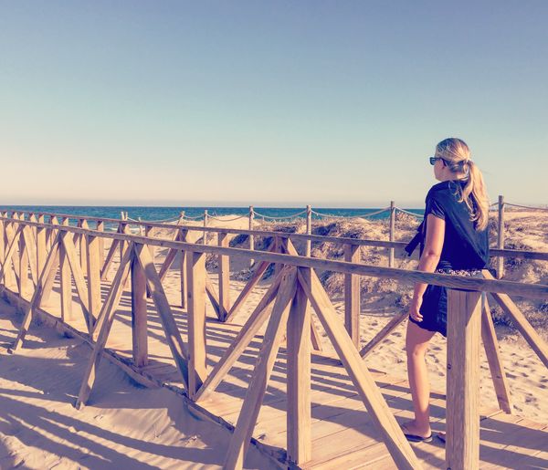 Rear view of woman walking on boardwalk at beach against sky