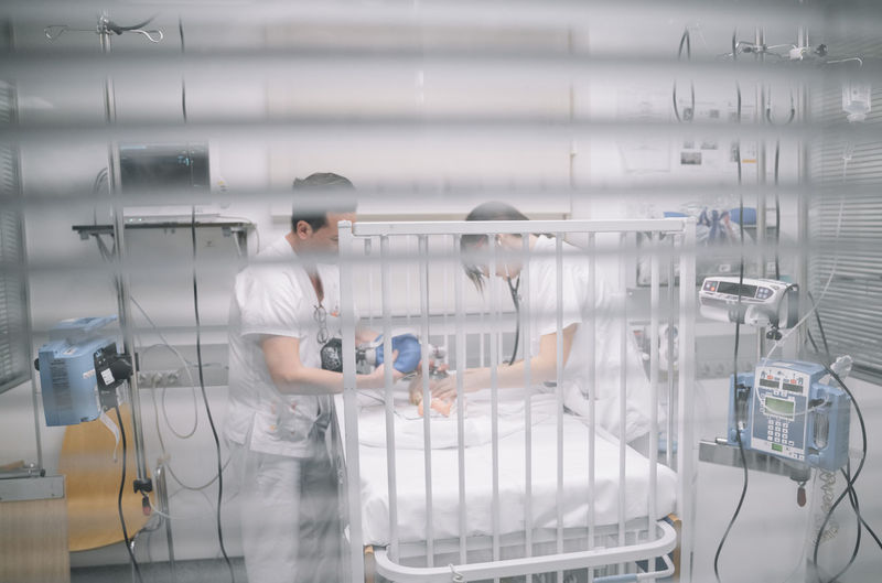 Faceless doctors standing near hospital bed with newborn in intensive care unit