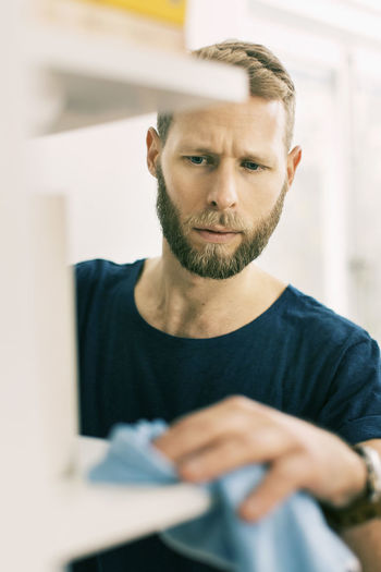 Man cleaning shelf with rag