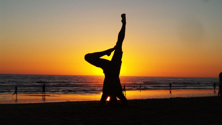 Silhouette woman with arms raised on beach against sky during sunset