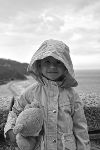 Portrait of smiling girl with teddy bear standing against sea