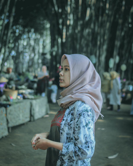 Teenage girl wearing hijab looking away while standing in city