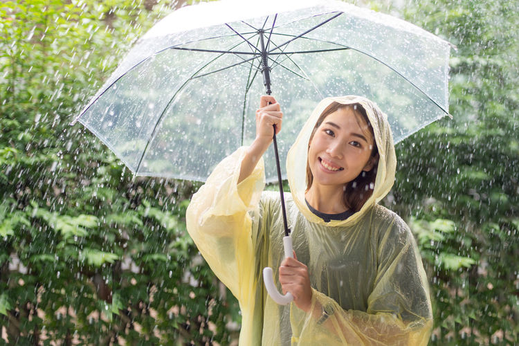 Portrait of smiling young woman holding umbrella in rain