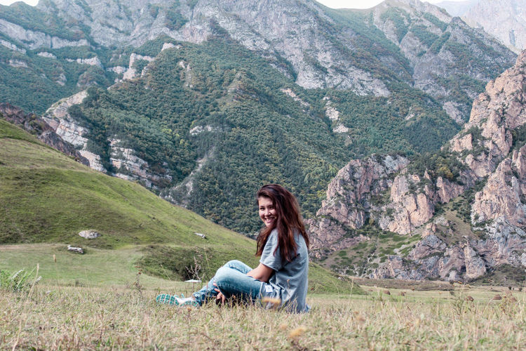 Side view of young woman sitting on field against mountain range