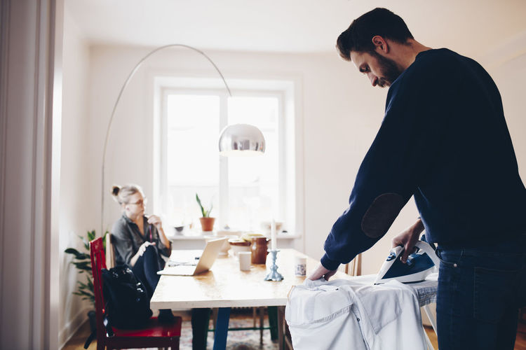 Man ironing while woman sitting on chair by dining table at home