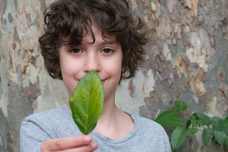 Portrait of boy holding leaf against wall