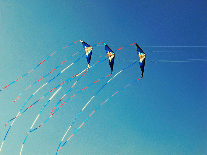 Low angle view of kites flying against clear blue sky