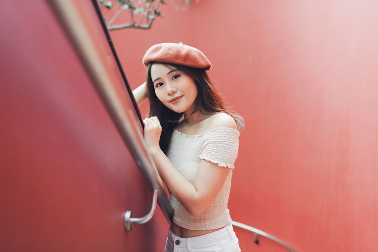 High angle portrait of young woman standing at railing against red wall
