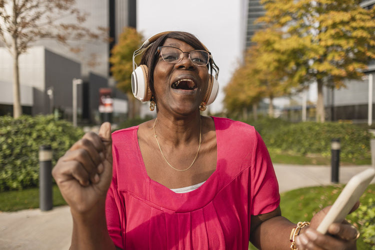 Happy woman wearing wireless headphones enjoying at park