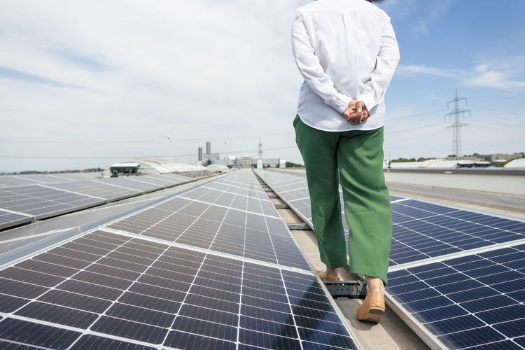 Businesswoman with hands clasped walking amidst solar panels on rooftop
