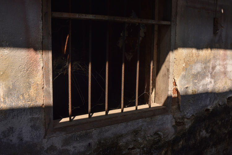 Sun shade lay across wooden window frame of an old house with security steel round bars.