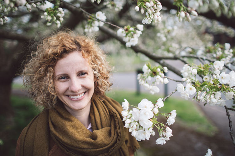 Portrait of smiling woman with curly hair by flowering tree