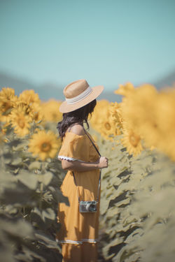 Side view of woman wearing hat standing in sunflower field against sky