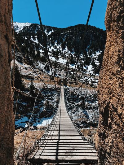 Footbridge leading towards mountain against clear sky during winter