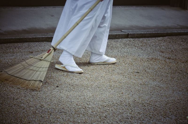 Low section of person cleaning footpath with broom
