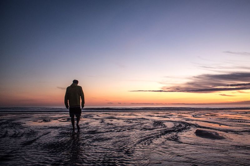 Rear view of man walking on beach at sunset