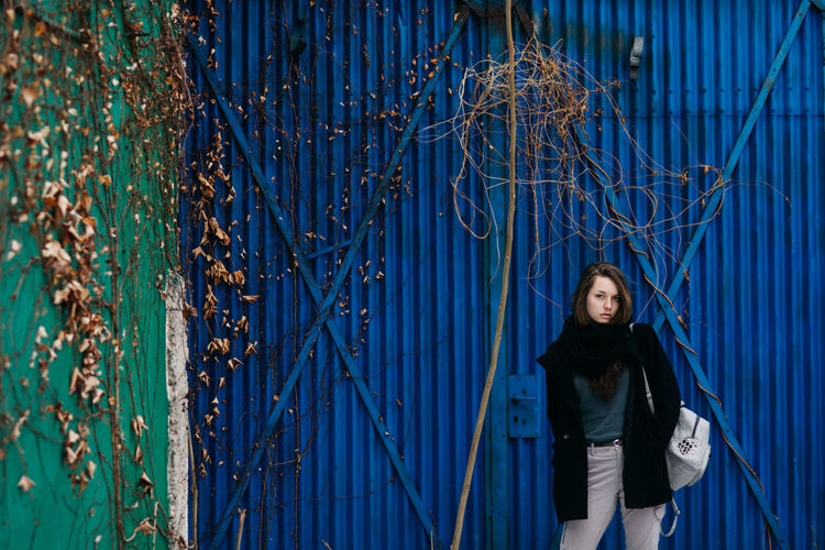 Portrait of young woman standing against blue corrugated iron