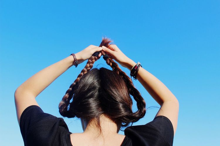 Woman holding braided hair up against clear sky