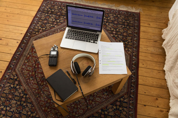 From above of audio recorder and headphones placed on wooden table with laptop and notebook for recording podcast at home