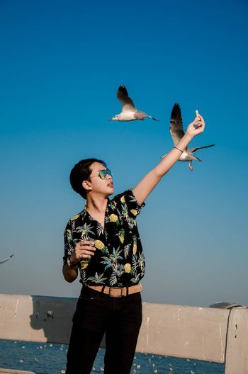 Man feeding birds against clear blue sky