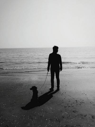Silhouette of man on beach with dog