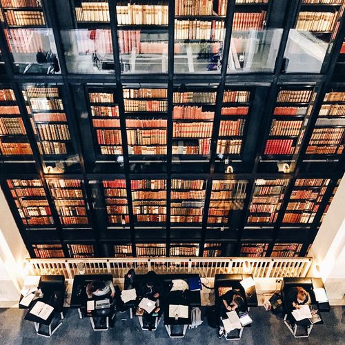Directly above shot of people reading books against bookshelf at british library