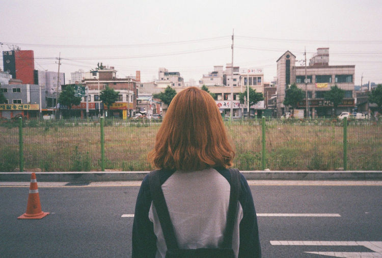 Rear view of woman standing on road against cityscape