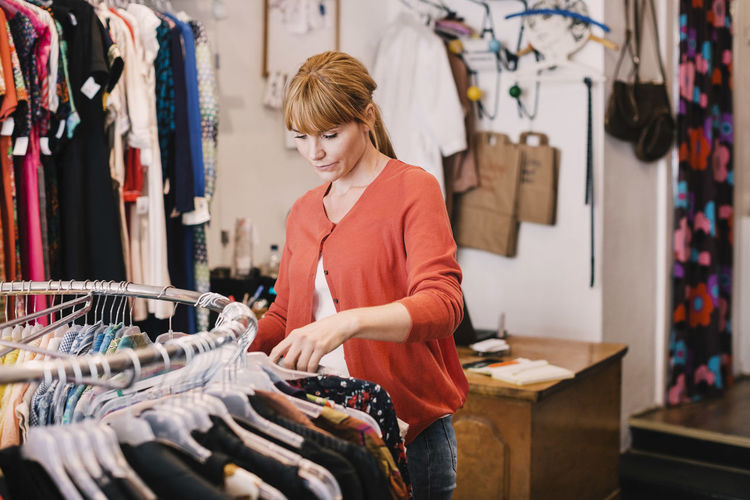 Owner arranging clothes on rack while standing at thrift store
