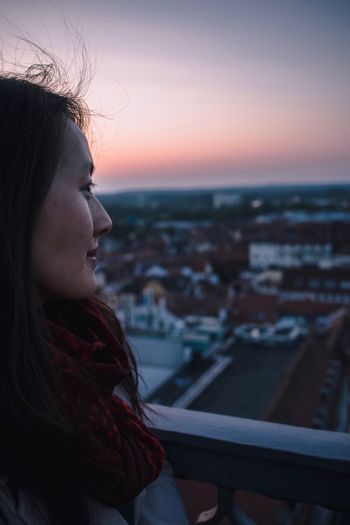 Woman looking at city against sky during sunset