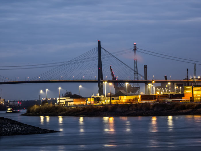 Illuminated bridge over river against sky in city