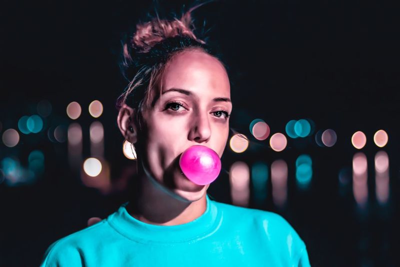 Portrait of young woman blowing bubble at night