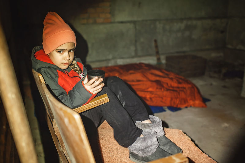 Ukrainian girl sits in bomb shelter, drinks tea and waits for end of airstrike of russian invaders