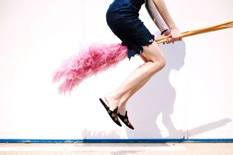 Low section of woman on broom against white wall