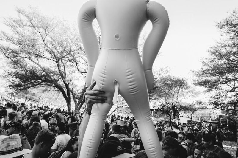 Cropped hand holding dummy in crowd during event against sky