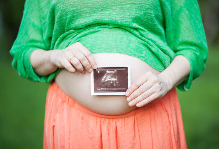 Midsection of pregnant woman holding ultrasound while standing outdoors