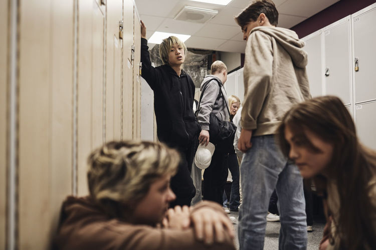 Teenage boy looking at girls talking with each other in school corridor