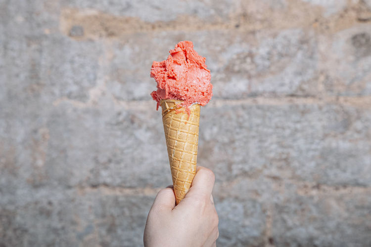 Hand holding strawberry flavor artisan ice cream cone. strawberry ice cream served in a waffle cone. 