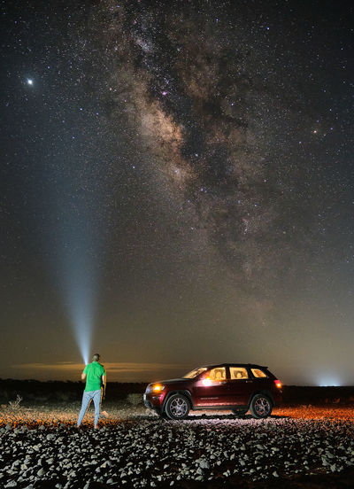 Man standing on car against sky at night