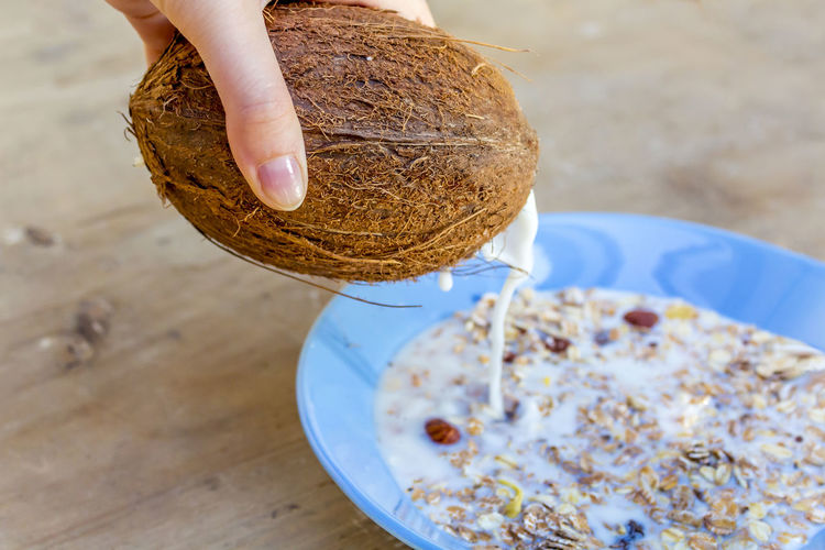 Cropped hand pouring coconut milk on muesli in plate at table