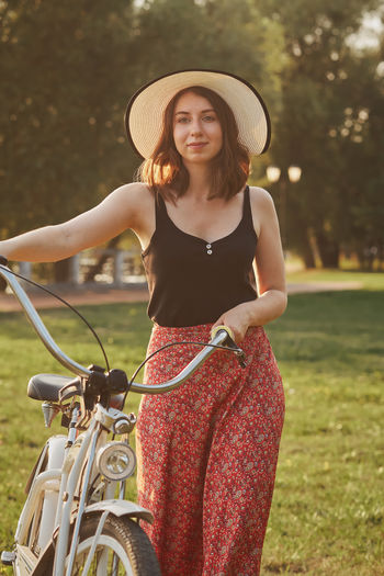 Smiling young woman holding bicycle walking in park