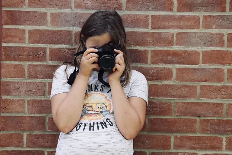 Full length of woman photographing against brick wall