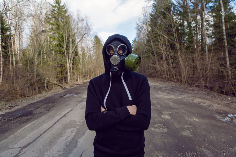Guy stands in a post apocalyptic forest during the day wearing a gas mask during a coronavirus 