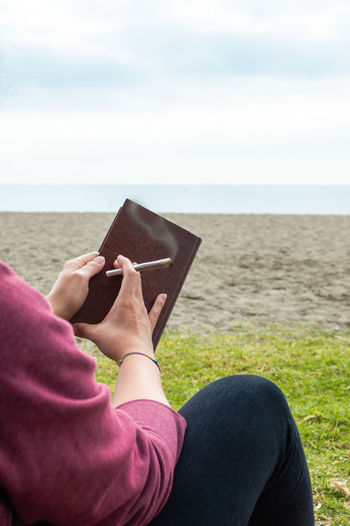 Midsection of man reading book on beach against sky