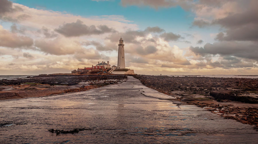 Lighthouse by sea against sky during sunset